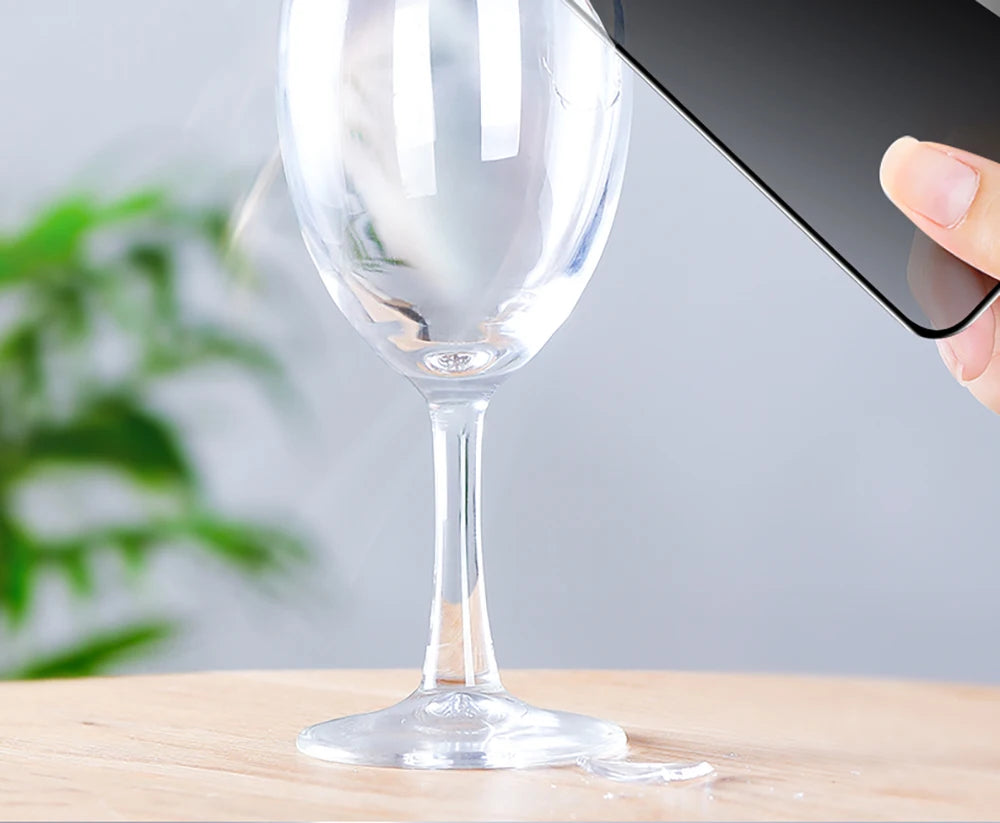 TrevioMart privacy screen protector for iPhone 14 Pro Max held next to a clear wine glass on wooden surface